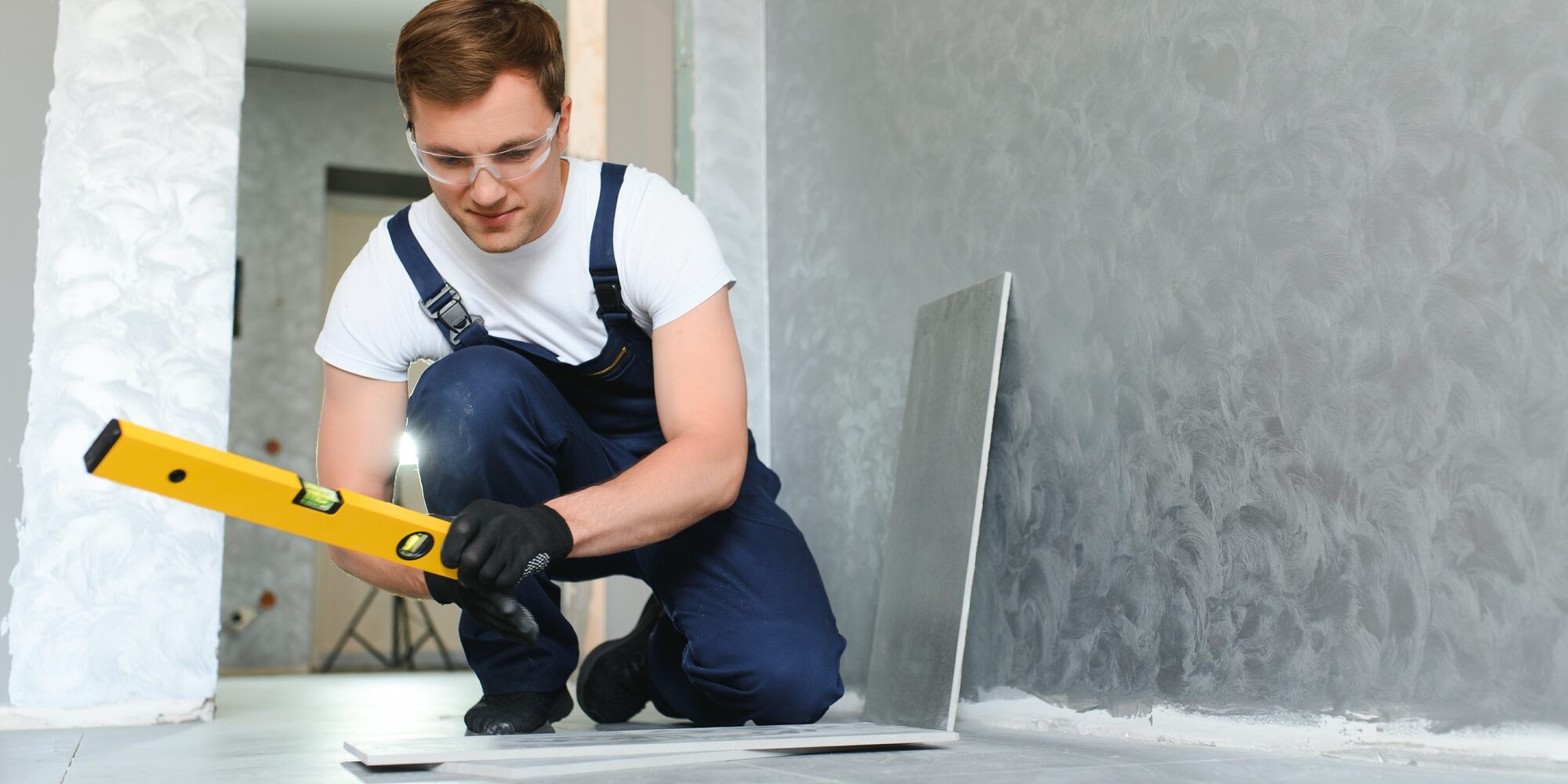Worker installing ceramic tile on floor near wall